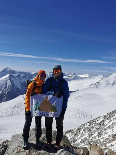 Two climbers holding the Nur Altai Tour flag on a snowy Altai summit