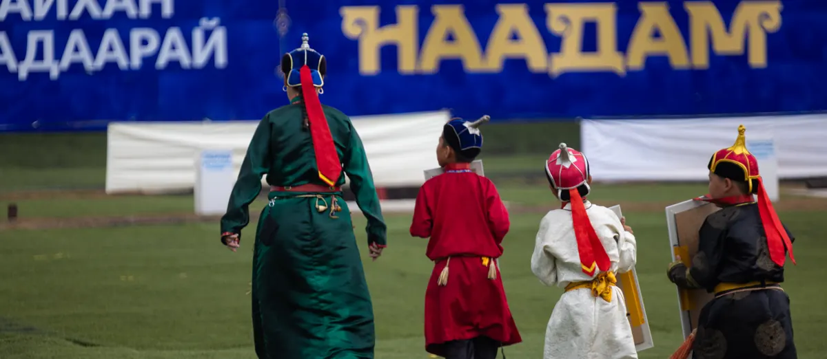 Wrestlers in traditional dress walking in front of the Naadam banner