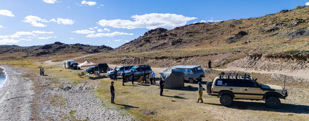 Nur Altai Tour team setting up camp with Land Cruisers beside a lake